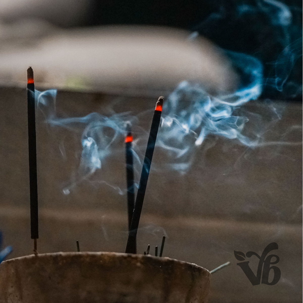 Incense sticks with smoke rising from a container, blurred background