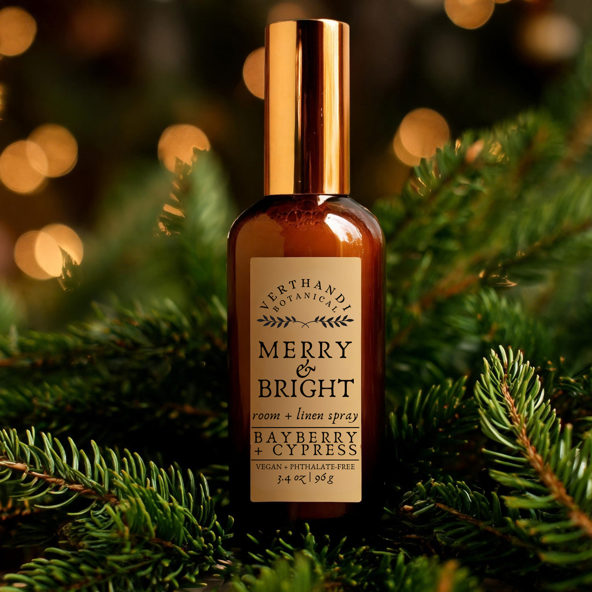 A bottle of Verthandi Botanicals Merry &amp; Bright room and linen spray, featuring a warm amber glass body and a metallic gold cap, set against a festive background of pine branches and warm bokeh lights.